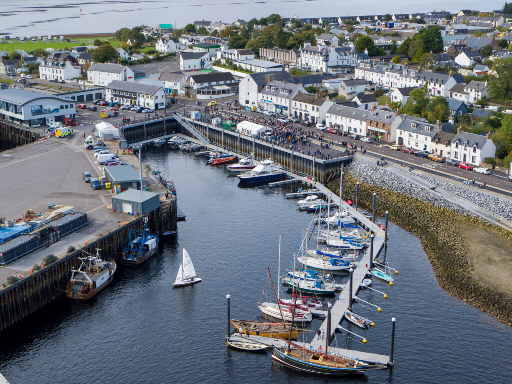 Aerial view of Ullapool harbour, with boats moored in the marina and the waterfront town beyond.