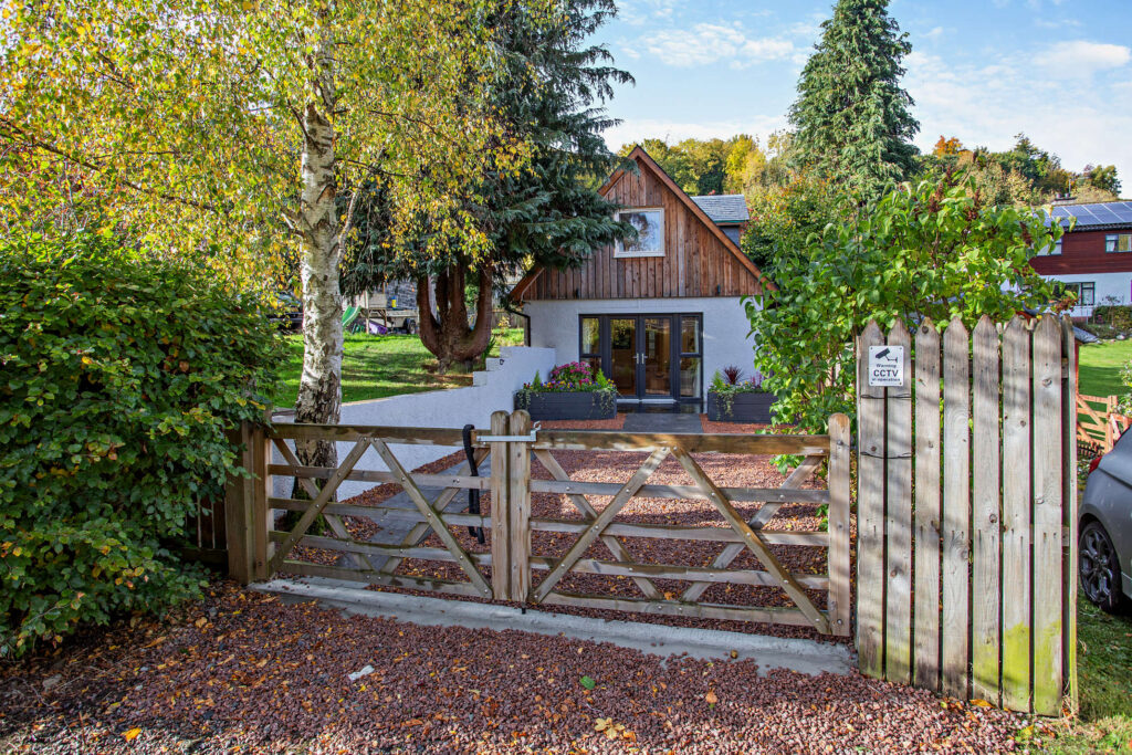 View of Highfield Lodge from the entrance gate showing the private gravel driveway and timber-clad exterior.