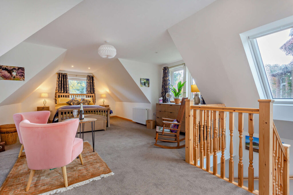 First-floor bedroom and seating area at Highfield Lodge with sloping ceiling, king bed and rocking chair.
