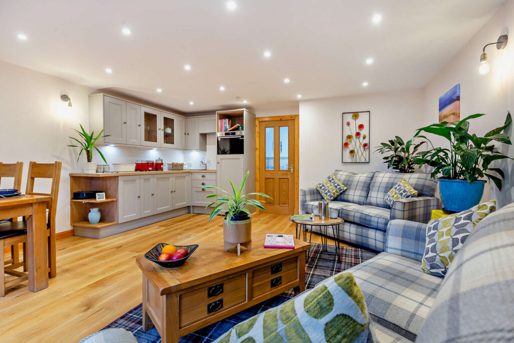 Open-plan living area at Highfield Lodge with kitchen, dining table, two tartan sofas and oak flooring.