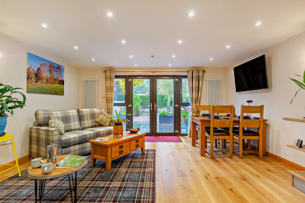 Open-plan sitting and dining area at Highfield Lodge with tartan sofas, coffee table, dining table and French doors to the patio.