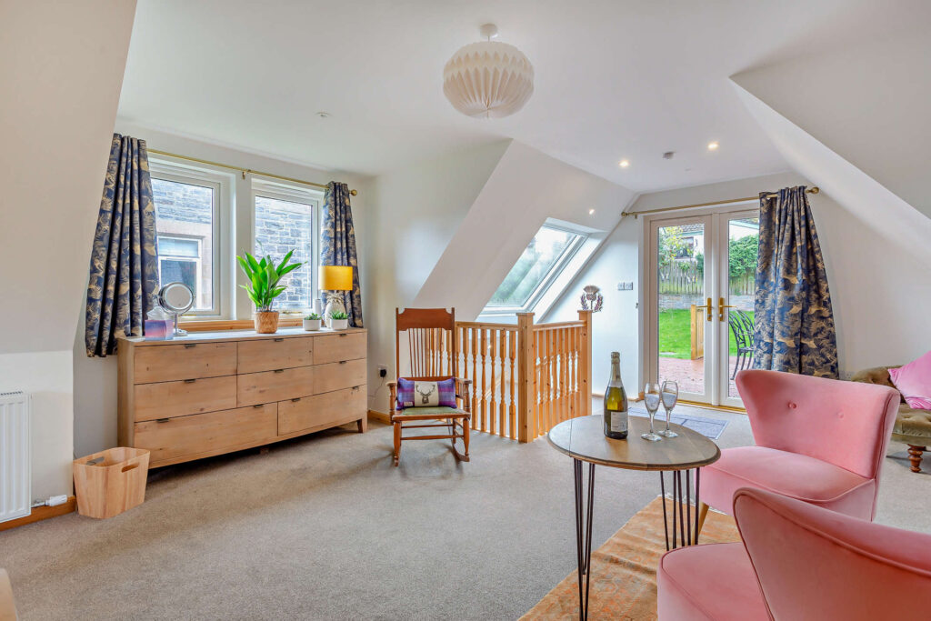 Spacious first-floor bedroom and sitting area at Highfield Lodge with king bed, pink armchairs and French doors to the deck.