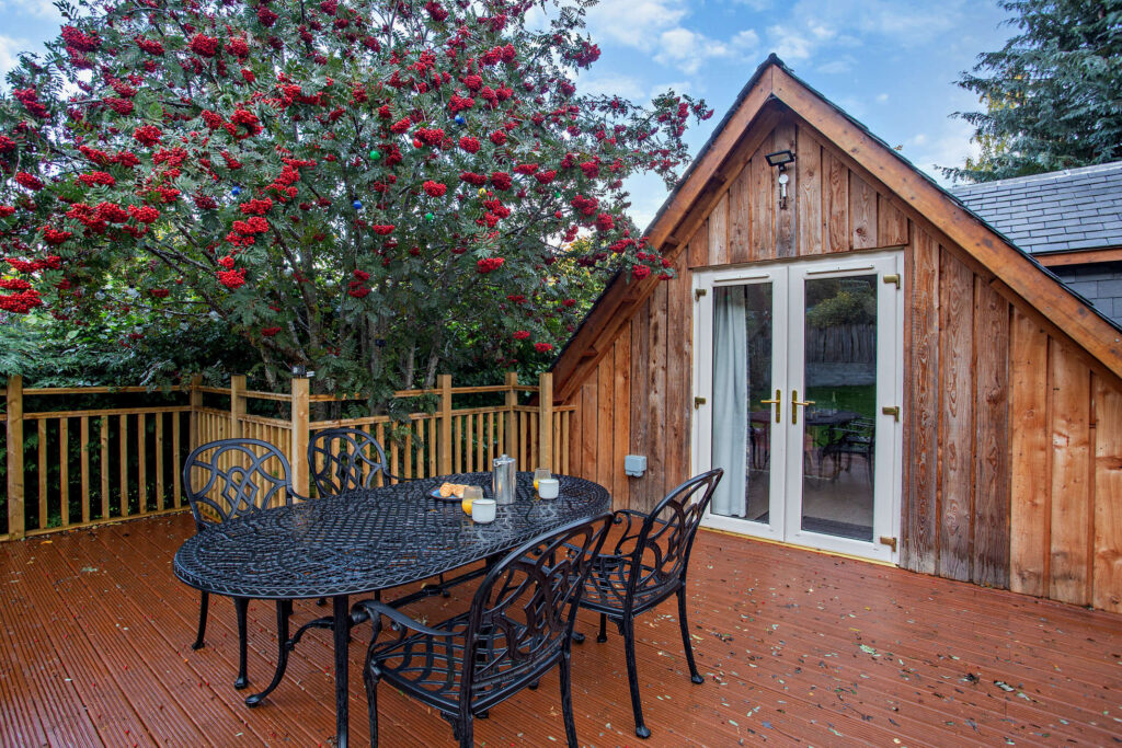 Timber deck at Highfield Lodge with outdoor dining table beside the lodge and mature rowan tree.