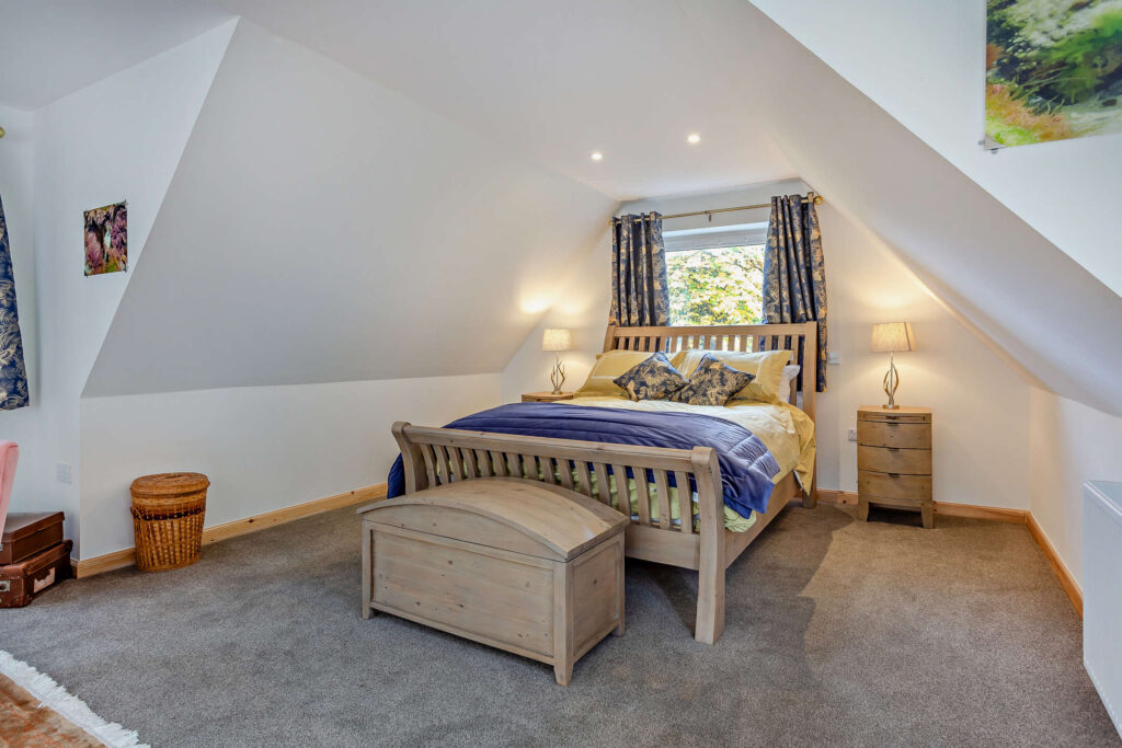 First-floor king bedroom at Highfield Lodge with sloping ceiling, wooden bed and soft neutral décor.