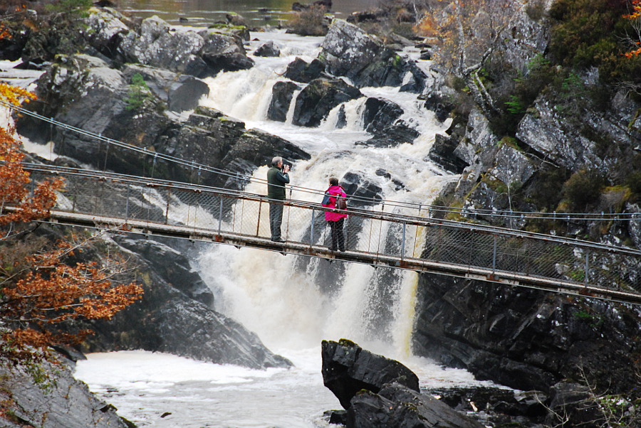 Rogie Falls near Contin, with visitors standing on the suspension bridge above the rushing waterfall.