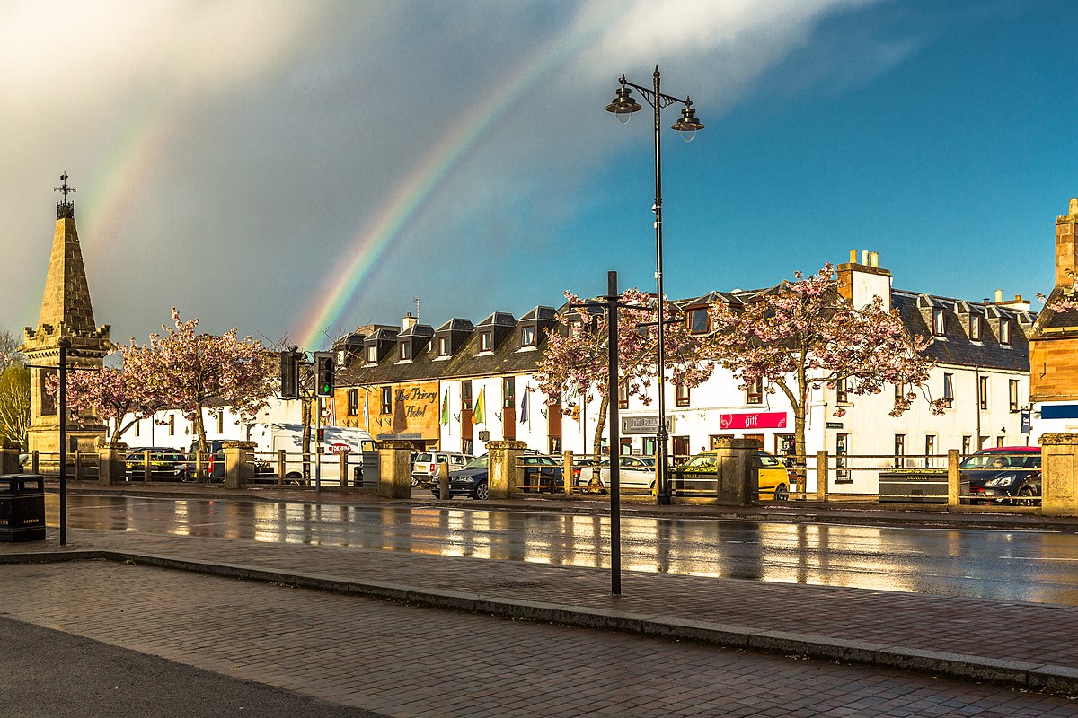 View across Beauly Square in Beauly, with cherry trees, shops and a rainbow after rain.