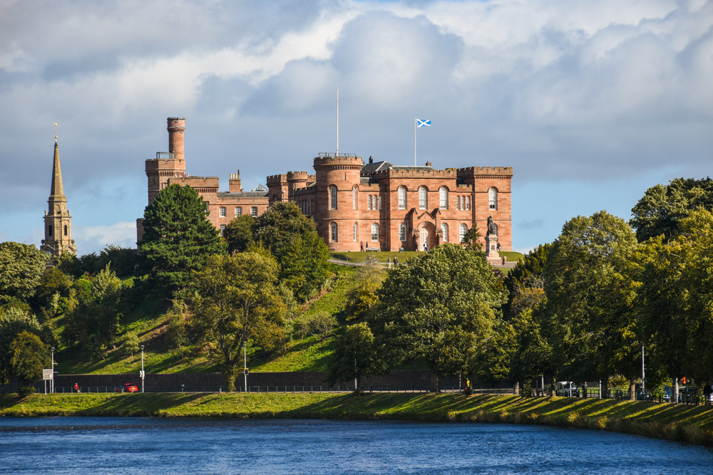 Inverness Castle on its hill above the River Ness, seen across the water from the opposite bank.