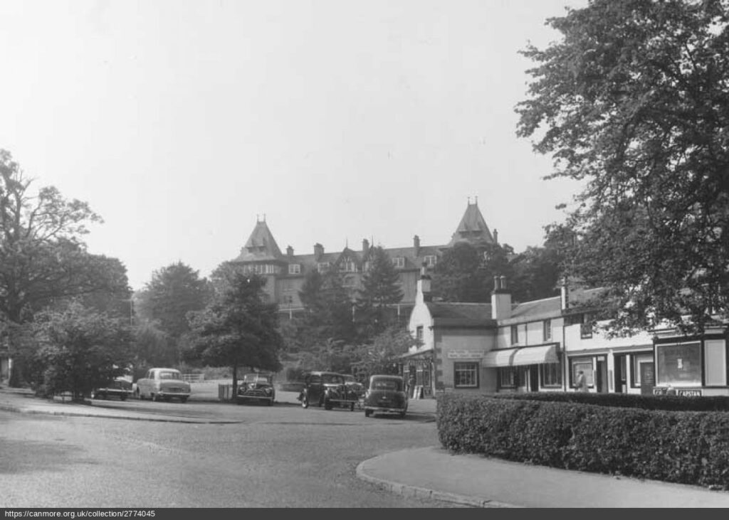 Black and white photograph of the Square in Strathpeffer in 1959, with the Highland Hotel on the hill in the background and shops in the foreground.